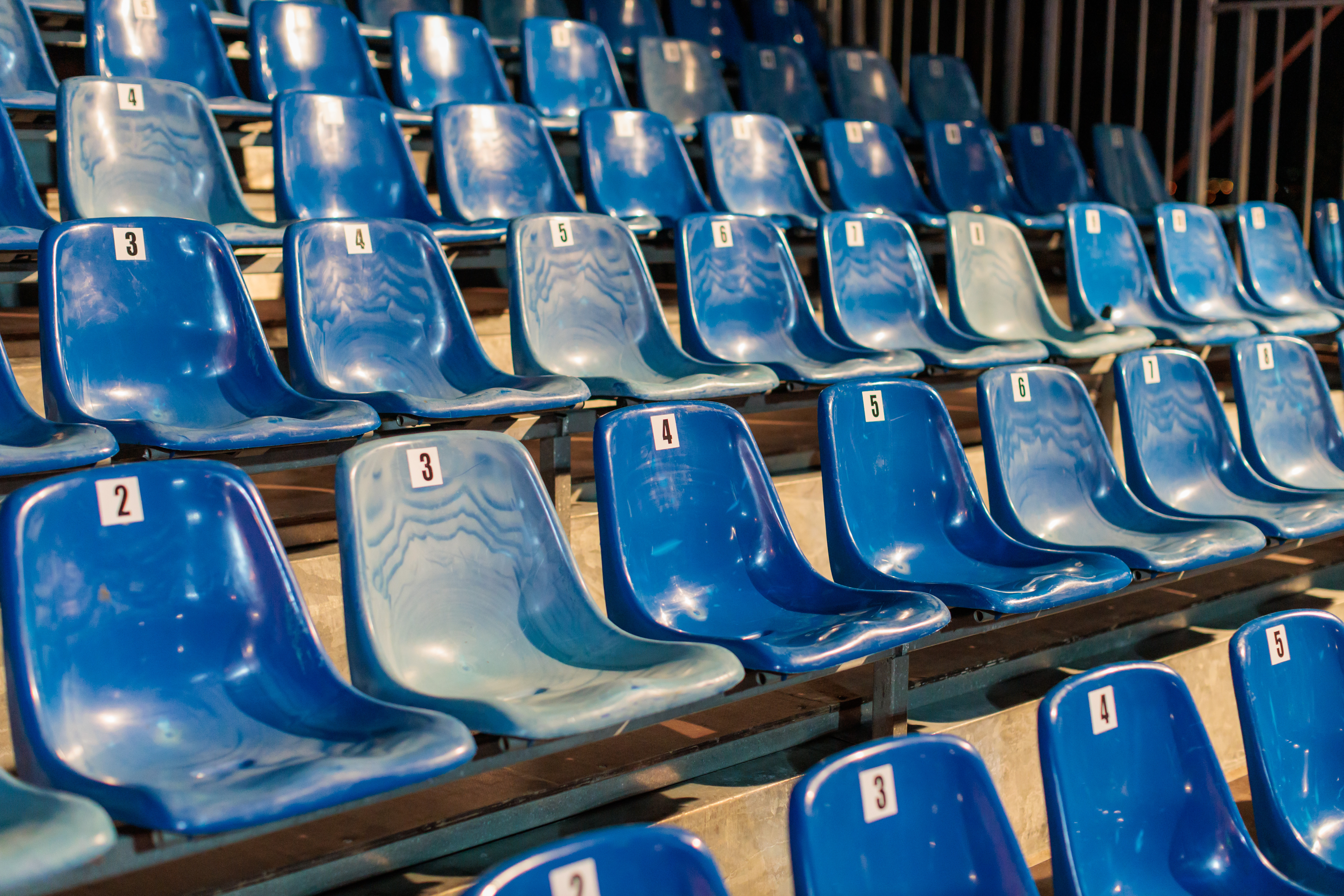 Rows of empty blue spectator seats in a sports arena, lit by afternoon sunlight